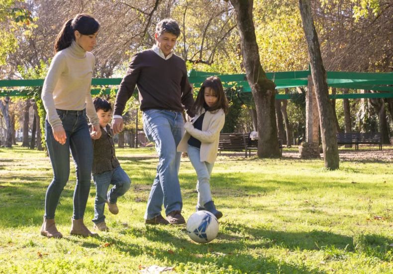 A family plays soccer together in a sunny park, enjoying quality time outdoors.